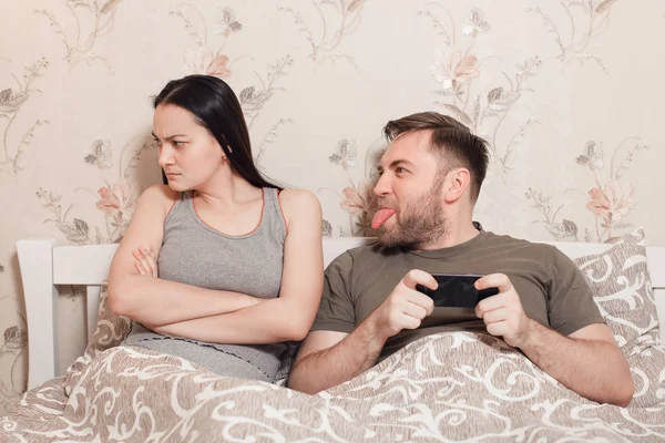 Hombre con teléfono burlas mujer en el dormitorio —  Fotos de Stock