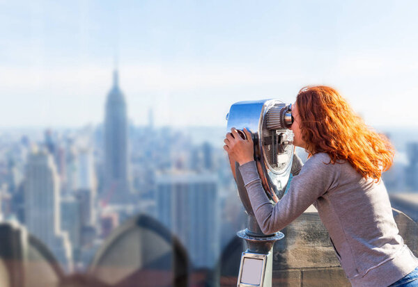 Young woman looking at the panorama of the city through an observation coin operated binoculars