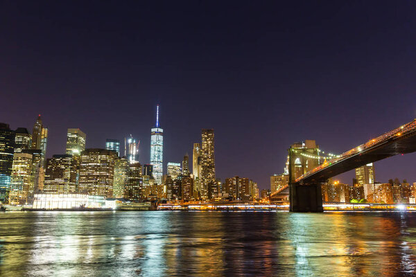 Illuminated Brooklyn bridge and Manhattan waterfront, view from Hudson river at night time, New York City, USA