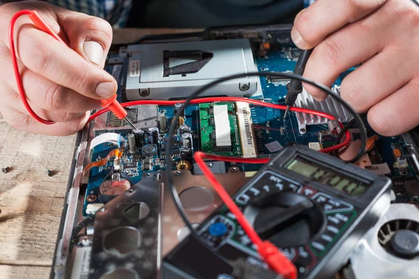 Engenheiro fazendo diagnósticos de laptop com multímetro — Fotografia de Stock