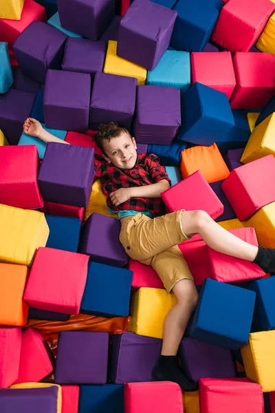 Мальчик лежит в куче разноцветных кубиков — стоковое фото