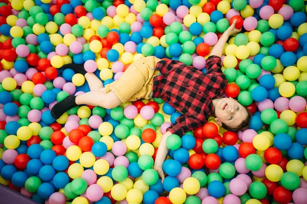 Menino deitado em pilha de bolas coloridas — Fotografia de Stock