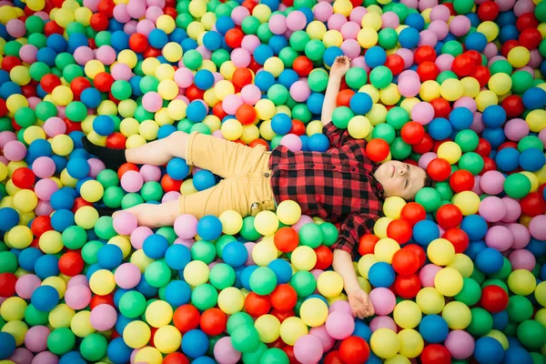 Kluk leží v hromadu barevných kuliček — Stock fotografie
