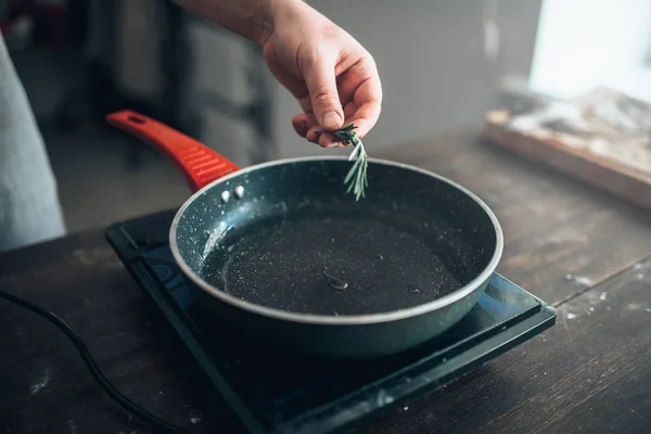 Шеф-повар кладет розмарин на сковородку — стоковое фото