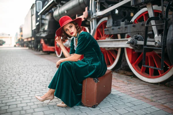 Mujer sentada en una maleta contra un tren de vapor —  Fotos de Stock