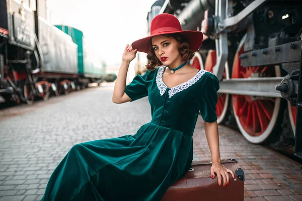 Mujer sentada en una maleta contra un tren de vapor —  Fotos de Stock