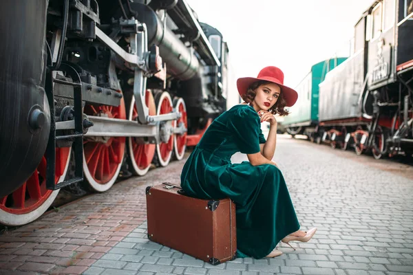 Vrouw zittend op koffer agaisnt stoomtrein — Stockfoto