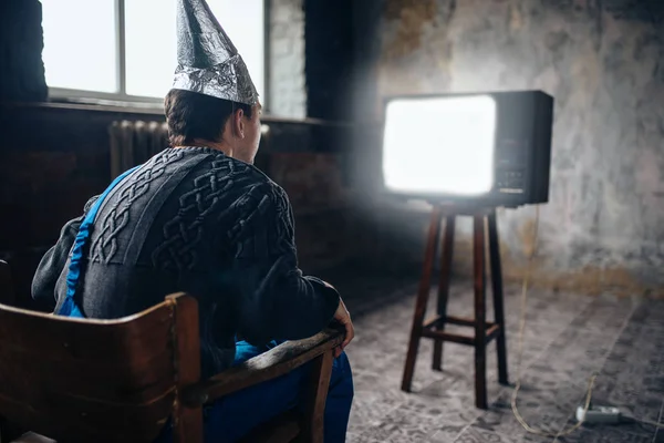 Человек в шлеме фольги смотрит телевизор — стоковое фото