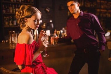 Kırmızı elbise onun yanında ayakta sayaç, yakışıklı adam bar kokteyl içme içinde çekici genç kadın. Gece kulübü, barda çekici çift Tarih 