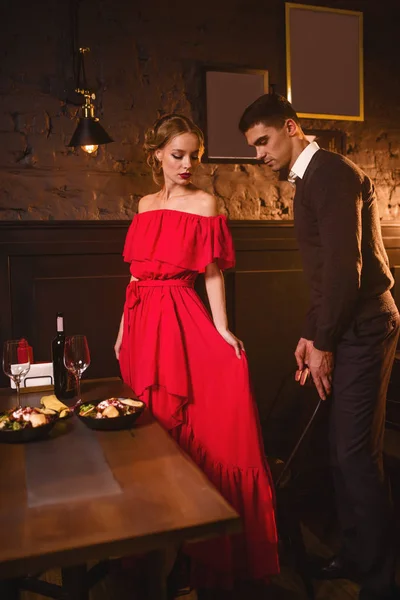 年轻的情侣在餐厅 浪漫的约会 优雅的女人穿着红衣服 英俊的男人帮她坐下 — 图库照片