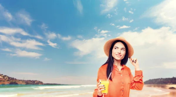 海岸にオレンジ ジュースを飲んでシャツと麦わら帽子で陽気な若い女性 — ストック写真