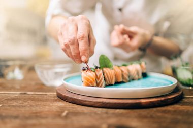 erkek aşçı dekorasyon suşi rulo mavi plaka üzerinde. Geleneksel Japon mutfağı, deniz ürünleri