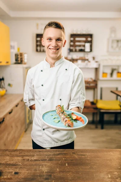 Homem Sorrindo Cozinheiro Segurando Rolo Sushi Placa Azul Cozinha Japonesa — Fotografia de Stock