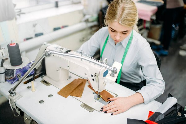 female dressmaker sewing on serger machine. Tailoring or dressmaking on clothing factory, needlework or sewing, seamstress in workshop