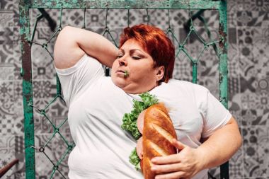 fat woman on bed eating sandwich, unhealthy lifestyle and obesity concept clipart