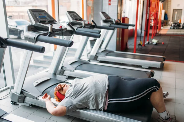 fat tired woman lying on treadmill after running in gym