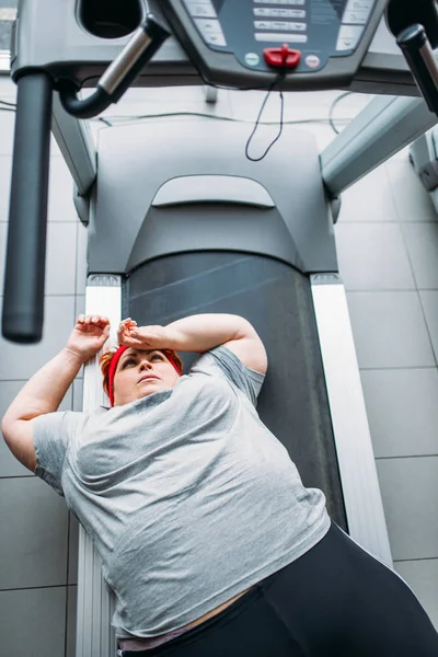 fat tired woman lying on treadmill after running in gym