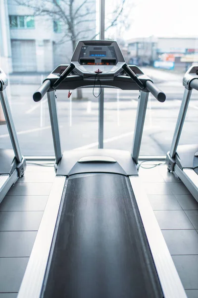 Treadmill machine against big window, gym interior, jogging track, stationary running simulator, sport equipment