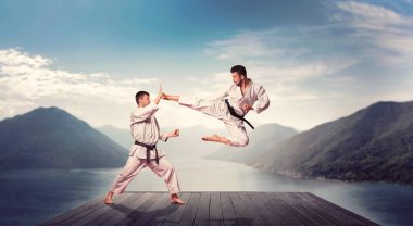 Martial arts karate masters in white kimono and black belts, fight training at pier, kick in jump clipart