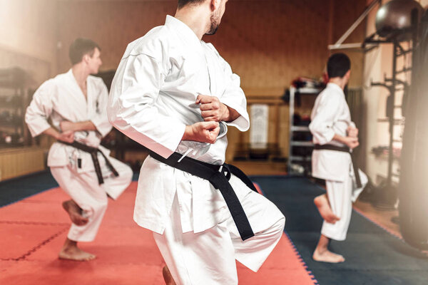 Martial arts karate master and disciples in white uniform and black belts, fight training in gym
