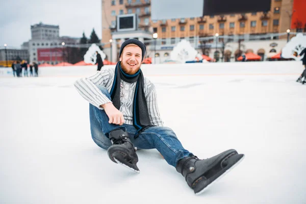 若いスケート リンクでスケートが氷の上に座っている男の笑みを浮かべて — ストック写真