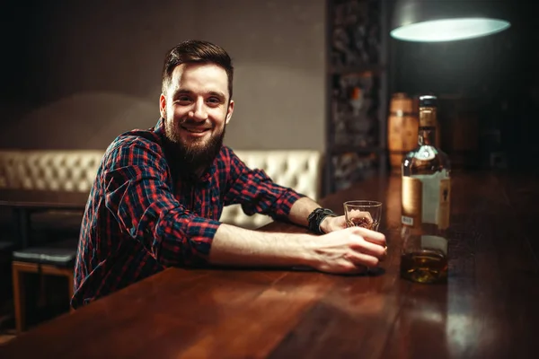 happy young man with bottle of whiskey at bar counter, alcoholism,  drunkenness concept