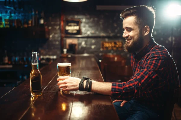 young bearded man drinking beer at bar counter in pub