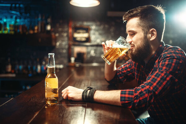 young bearded man drinking beer at bar counter in pub