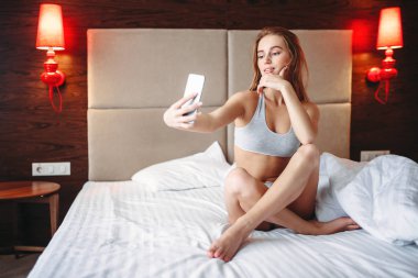 Çekici kadın yatakta oturmuş ve selfie yapım telefon üzerinde iç çamaşırı
