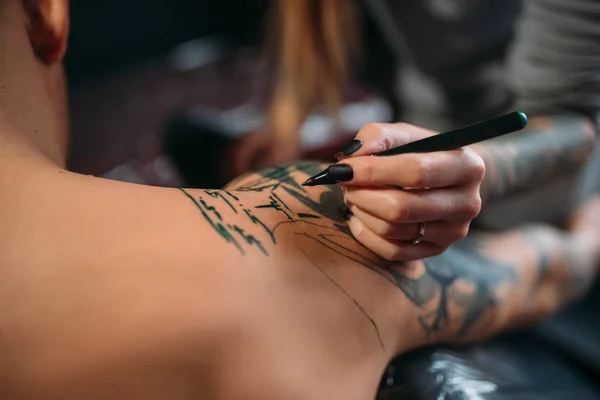 female tattooist making tattoo by machine on male shoulder. Professional tattooing in salon