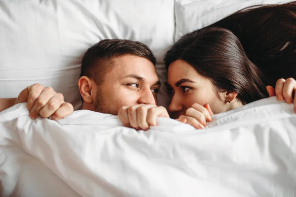shy love couple lying on big white bed, intimate partners in bedroom