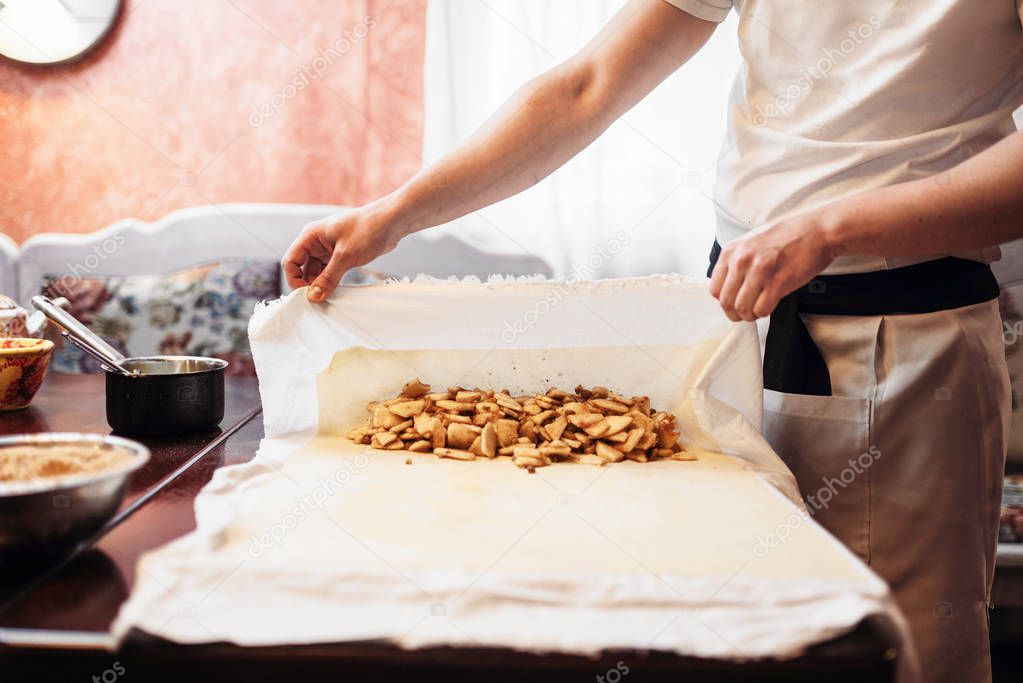 male chef wrapping filling into dough, apple strudel cooking process, homemade sweet dessert