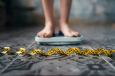 female feet on scales closeup, measuring tape, weight loss, hard dieting clipart
