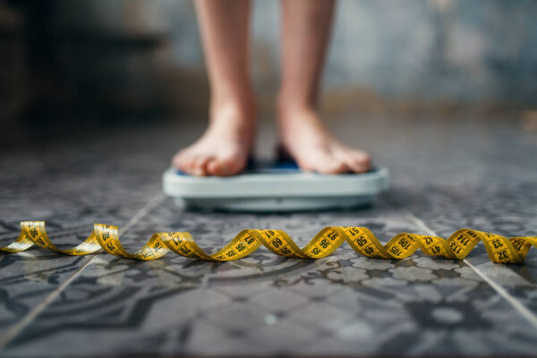female feet on scales closeup, measuring tape, weight loss, hard dieting