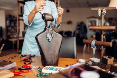 woman trying on handmade necklace on wooden mannequin, needlework clipart