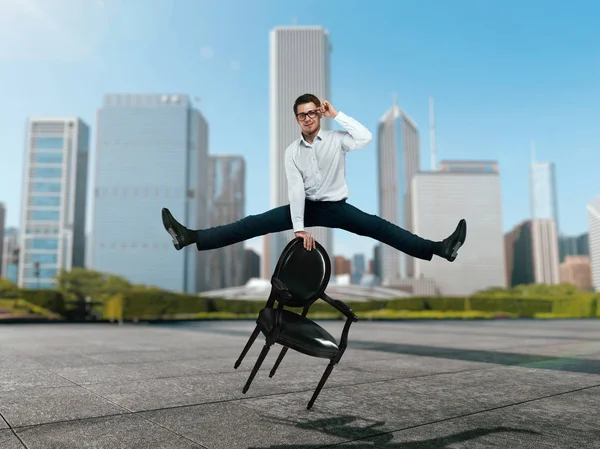 Joven Hombre Negocios Gafas Saltar Sobre Silla Contra Los Rascacielos — Foto de Stock