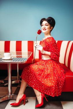 kadın kanepede oturan ve gül, retro Amerikan moda tutan poz gülümseyen PIN 