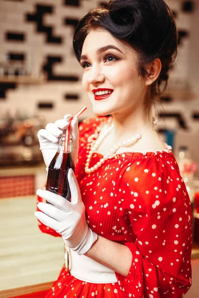 pinup woman drinking  carbonated drink in retro cafe, red dress with polka dots, vintage style