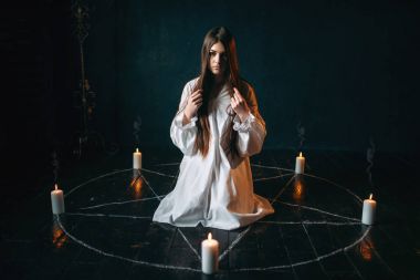 Beyaz gömlekli pentagram daireyle mumlar, kara büyü, siyah ahşap zemin ayini merkezinde oturan genç kadın