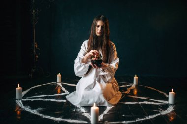 Beyaz gömlekli pentagram daireyle mumlar, kara büyü, siyah ahşap zemin ayini merkezinde oturan genç kadın