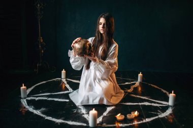 Beyaz tişörtlü insan kafatası pentagram daire içinde tutan genç kadın 