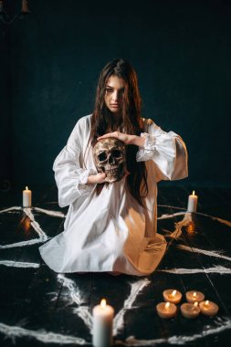 Beyaz tişörtlü insan kafatası pentagram daire içinde tutan genç kadın 