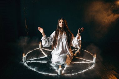 Beyaz gömlekli pentagram daireyle mumlar, kara büyü, siyah ahşap zemin ayini merkezinde oturan genç kadın
