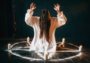 Beyaz gömlekli pentagram daireyle mumlar, kara büyü, siyah ahşap zemin ayini merkezinde oturan genç kadın