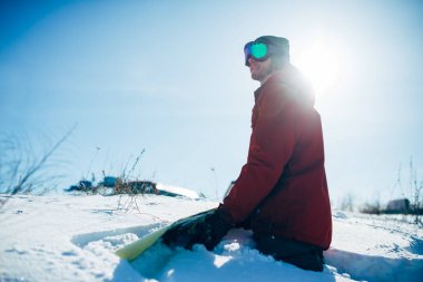 Snowboard karlı yamaçta güneşli bir günde oturan gözlüklü. Kış aşırı spor, aktif yaşam tarzı. Dağlarda snowboard