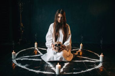 Beyaz tişörtlü insan kafatası pentagram daire içinde tutan genç kadın 