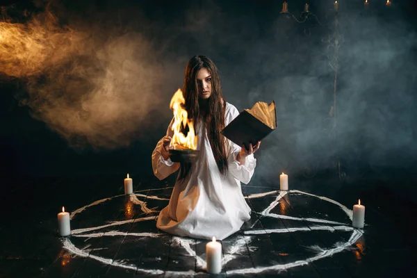 Mumlar ile pentagram dairenin merkezinde oturan ve okuma bir büyü, kara büyü ritüel, yöneltici Beyaz gömlekli genç kadın