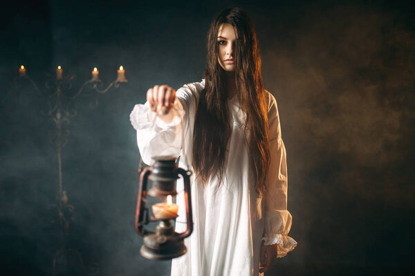 Woman in white shirt holding kerosene lamp, black magic ritual, occult and exorcism