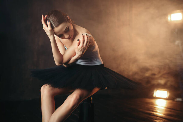 graceful and beautiful ballerina sitting on black banquette on the stage in theater