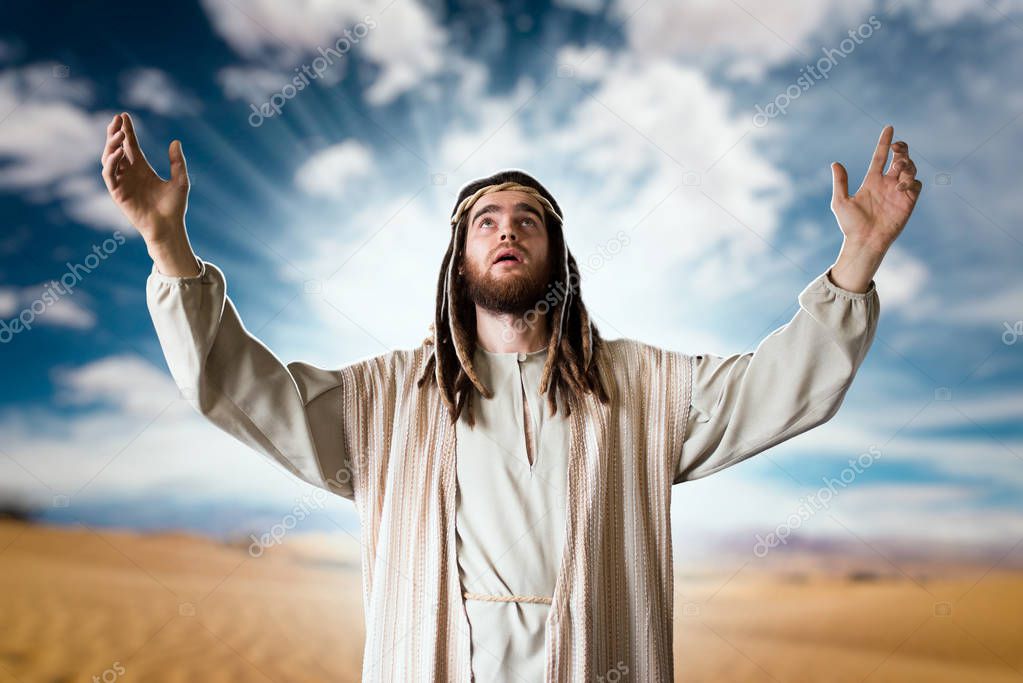 Jesus Christ in white robe praying with his hands up against cloudy sky. Strong faith in God, christianity